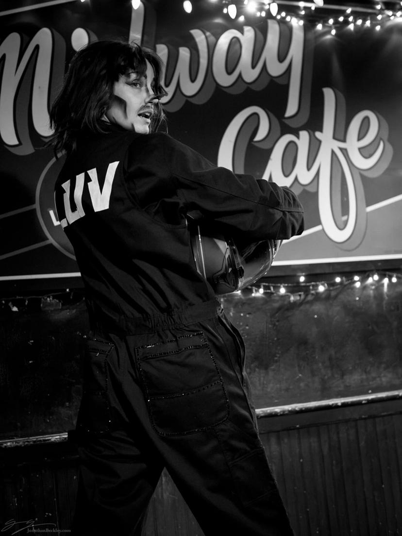 drag performer in a jumpsuit with LUV on the back, turning around to face the audience, holding their motorcycle helmet